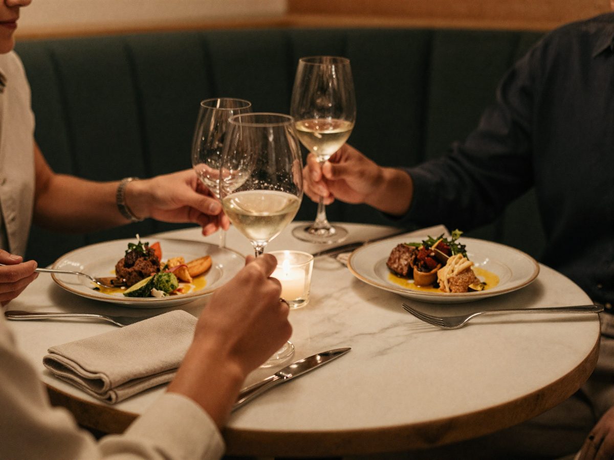 Guests mid-meal at a marble table, hands and glasses in warm light